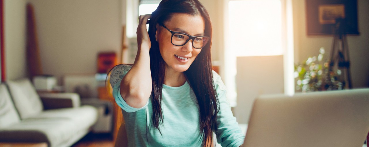 A female online social sciences degree student with glasses is sitting behind a laptop while attending core courses online.