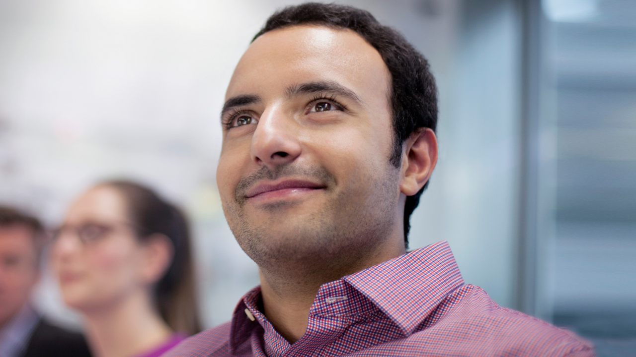 A leadership and management student is sitting in class while looking up and smiling.