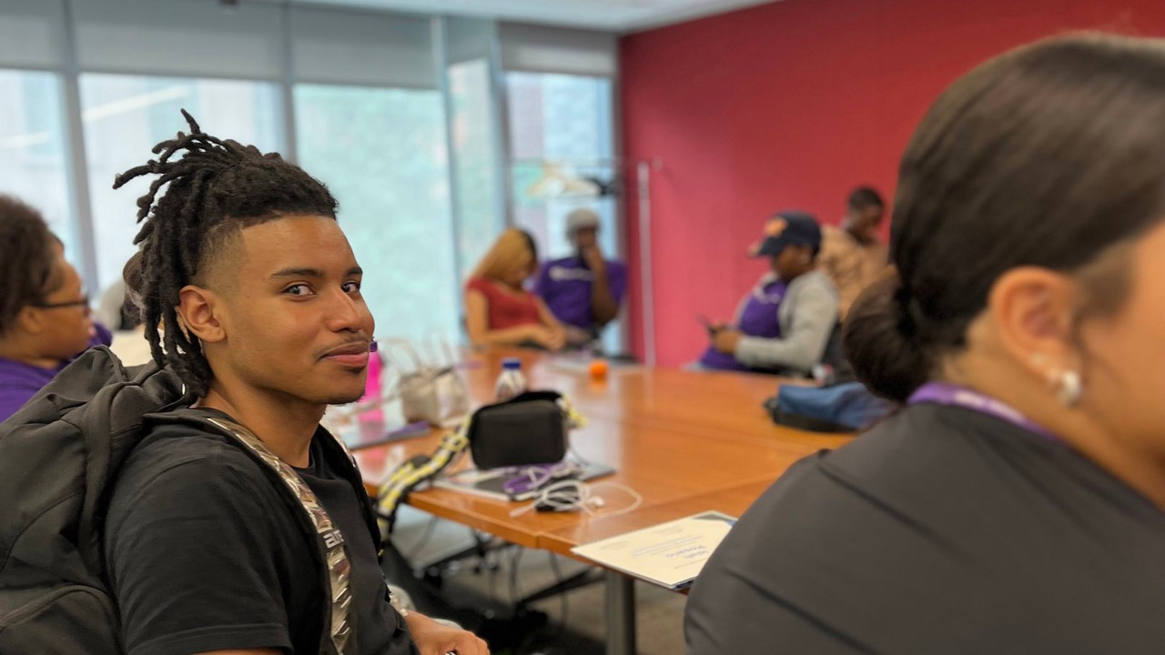 Student at desk with other students looking at camera